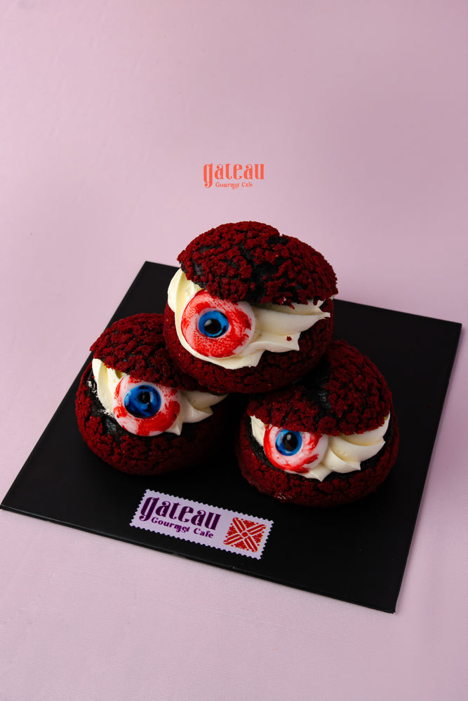 Three bloody eyes choux pastry topped with cream and decorative red cookies at Gateau Gourmet Cafe