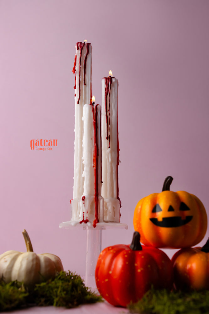 Spooky bloody Halloween candles dripping red wax, surrounded by decorative pumpkins at Gateau Gourmet Cafe