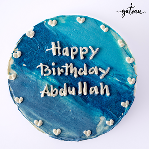Blue ombre cake with Happy Birthday Abdullah written in white icing and small heart decorations