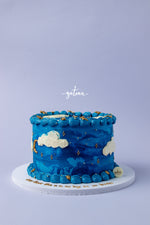 Blue sky cake design by Gateau Gourmet Cafe with blue frosting, white clouds, and gold star accents on a white cake board