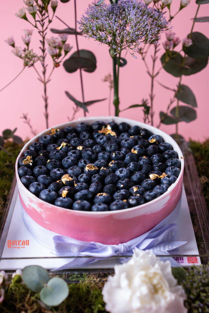 Gateau Gourmet Cafe blueberry cheesecake with floral arrangement topped with fresh blueberries and gold accents