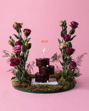 Gateau Gourmet Cafe chocolate cake with floral arrangement featuring purple and pink flowers on a green moss base