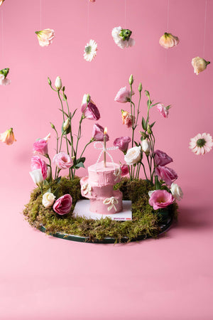 Gateau Gourmet Cafe cake with floral arrangement featuring pink flowers and green moss on pink background