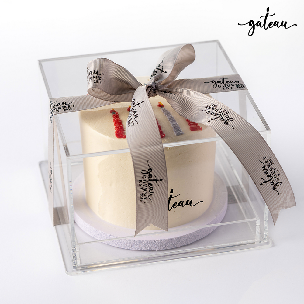 Gateau Gourmet Cafe candle bundle cake with white frosting in clear display box tied with a branded ribbon