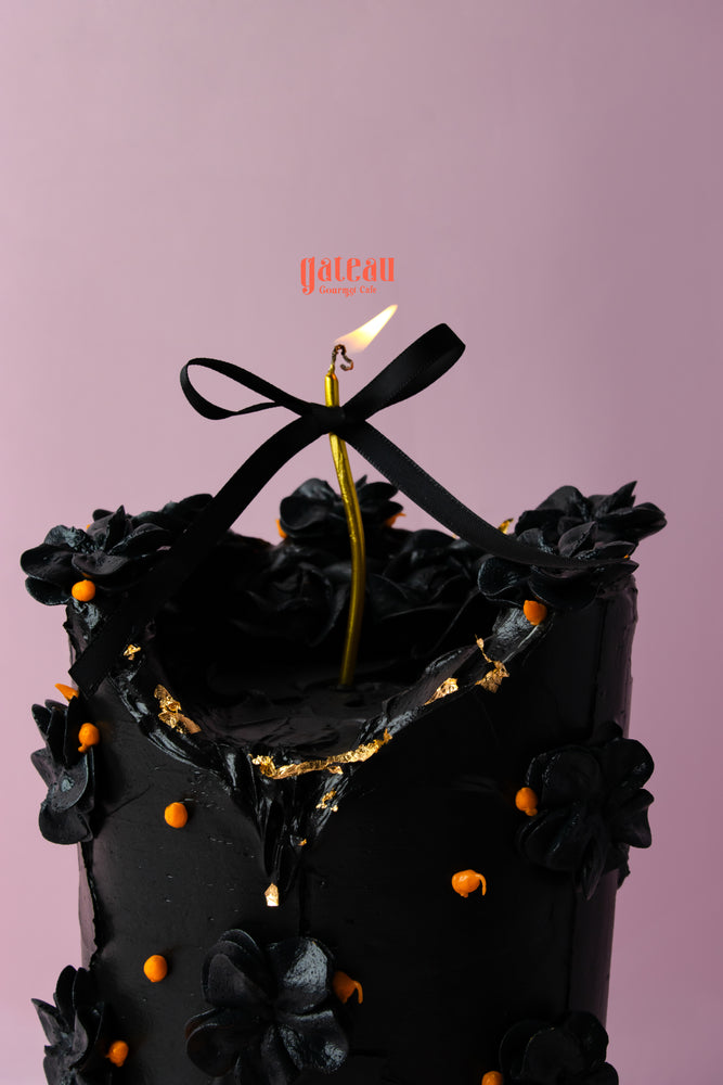 Elegant black candle cake for celebrations decorated with flowers and a ribbon at Gateau Gourmet Cafe