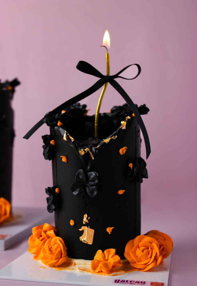 Elegant candle cake for celebrations featuring black floral decorations and a lit candle on top