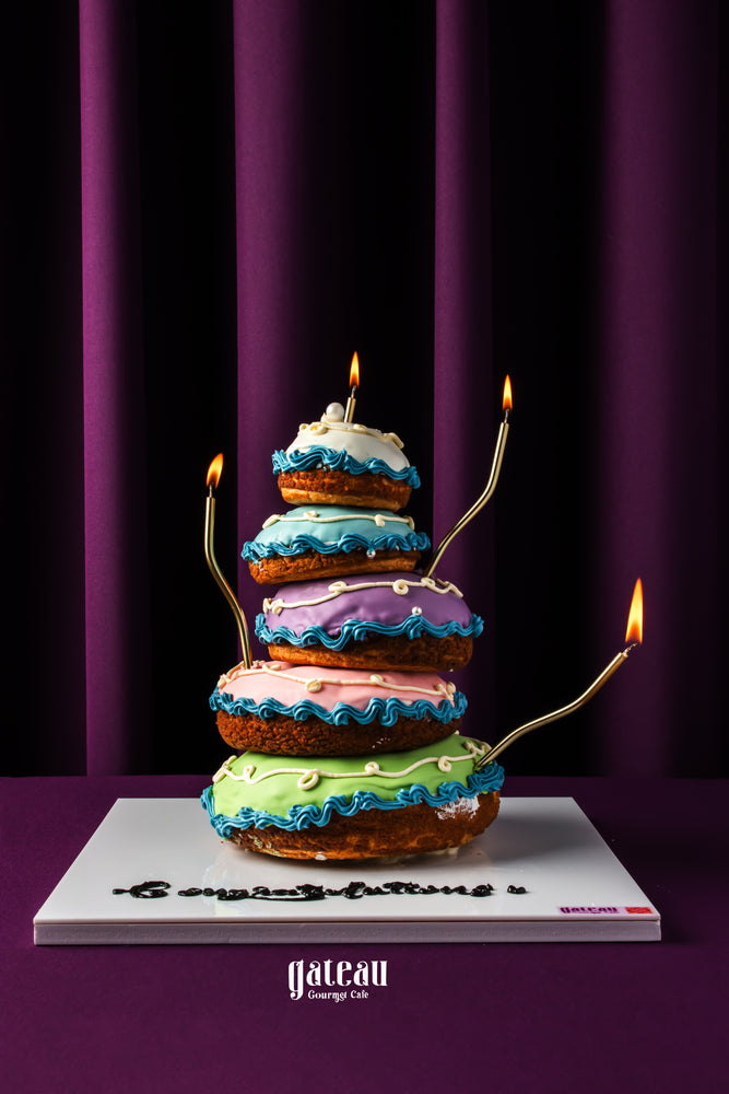 Colorful layered choux pastry cake with lit candles displayed on a choux pastry stand by Gateau Gourmet Cafe