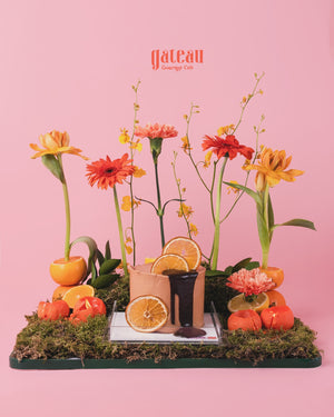 Citrus cake with fresh flowers displayed on moss with sliced oranges and vibrant blooms by Gateau Gourmet Cafe