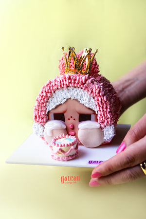 Gateau Gourmet Cafe CRYBABY character cake with pink frosting and gold crown on white serving board