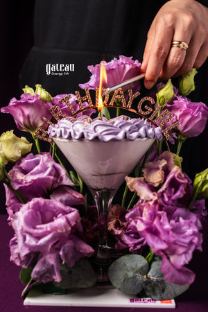 Custom birthday cakes for her by Gateau Gourmet Cafe with purple floral decoration and lit birthday candle
