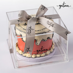 Beautiful custom colored cakes displayed in a clear box with elegant ribbon from Gateau Gourmet Cafe