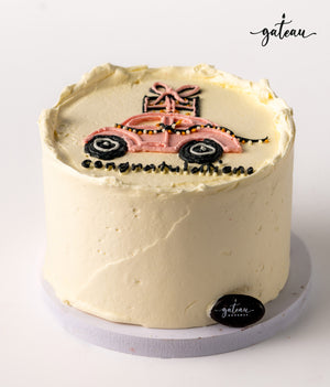 Custom new car cake decorated with pink icing and a gift on top from Gateau Gourmet Cafe