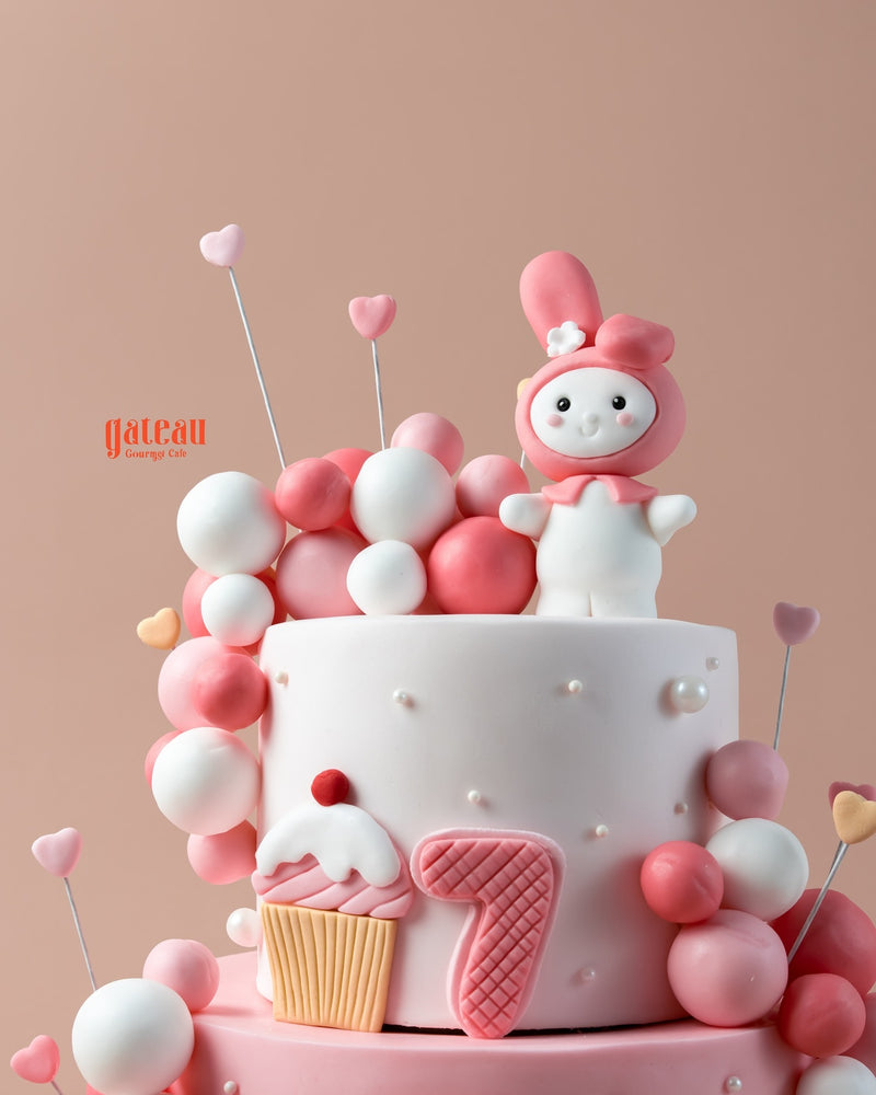 Custom pink birthday cake designed by Gateau Gourmet Cafe with cute decorations and a playful character