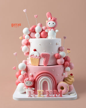 Custom pink birthday cake with fun decorations, balloons, and a cute character design by Gateau Gourmet Cafe
