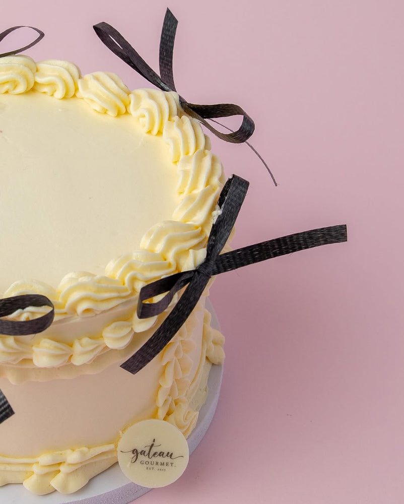 Custom royal cake design with creamy yellow frosting and black ribbon accents by Gateau Gourmet Cafe