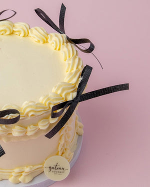 Custom royal cake design with creamy yellow frosting and black ribbon accents by Gateau Gourmet Cafe