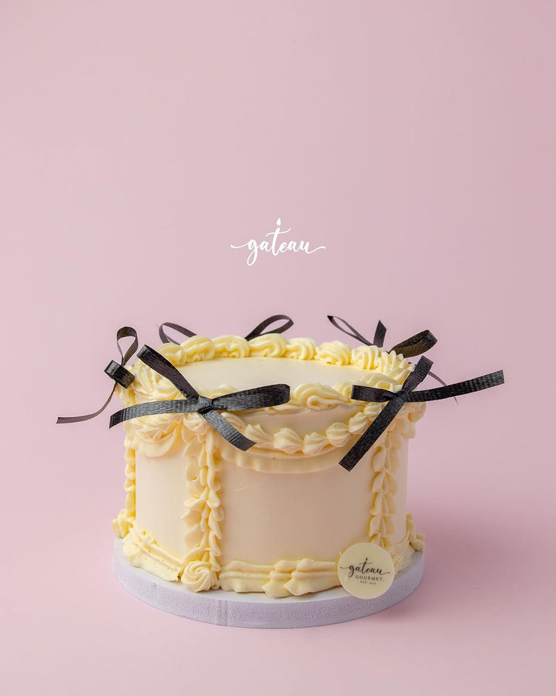 Gateau Gourmet Cafe custom royal cake design with yellow frosting and black ribbon bows on a pink background