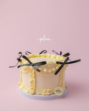 Gateau Gourmet Cafe custom royal cake design with yellow frosting and black ribbon bows on a pink background