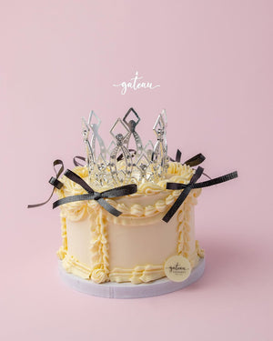 Gateau Gourmet Cafe custom royal cake design with cream frosting, black ribbon, and silver crown decoration