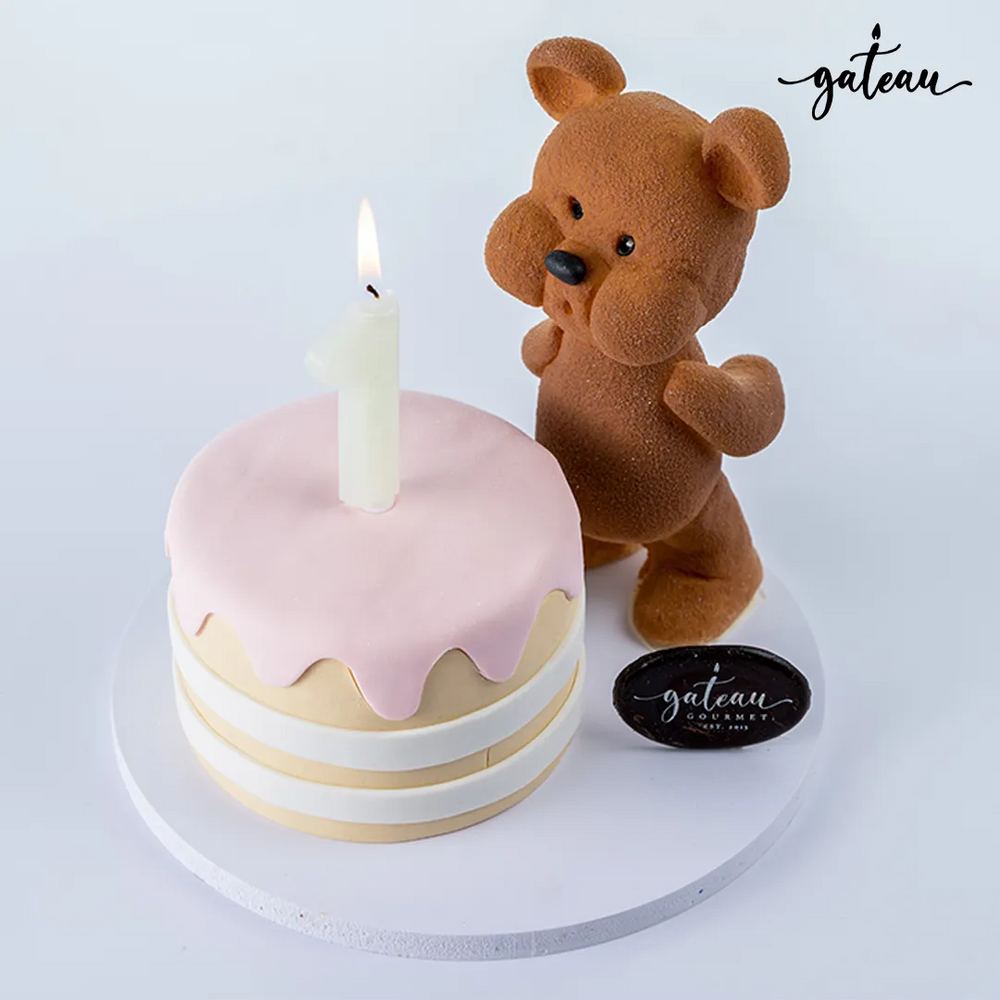 Custom teddy bear cake with pink frosting and a cute teddy bear figurine holding a candle