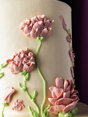 Close-up of custom wedding cake design with delicate pink flower frosting on white icing