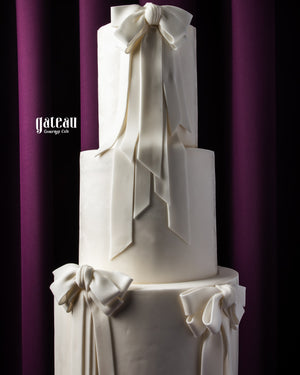 Elegant white three-tier custom wedding cakes with large decorative bows by Gateau Gourmet Cafe