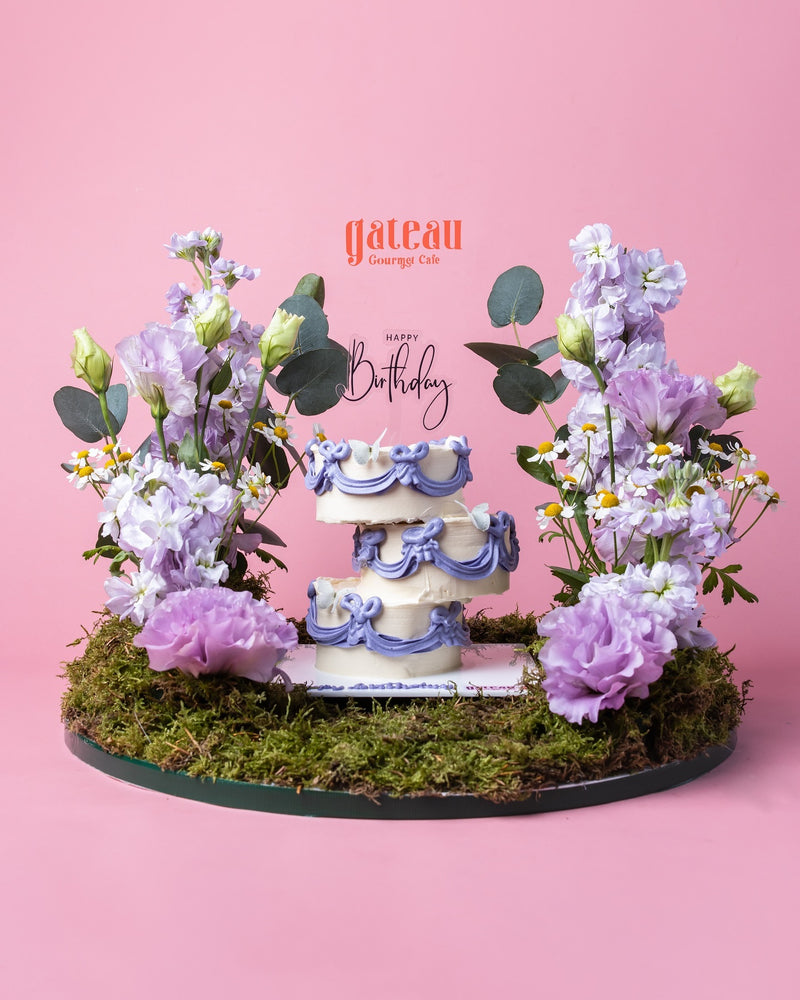 Gateau Gourmet Cafe decorative cake arrangement with purple floral decorations on moss base for birthday