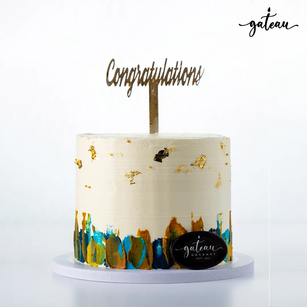 Gateau Gourmet Cafe decorative celebration cake with white frosting, gold accents, and congratulations topper