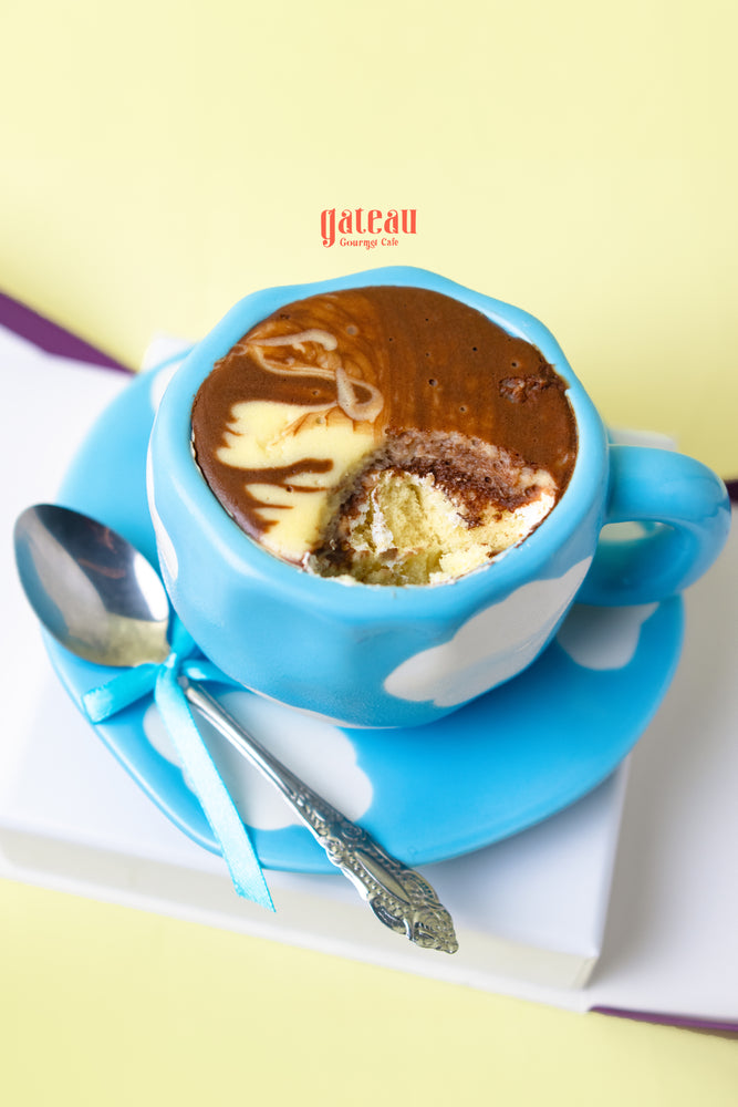 Decorative teacup cake in a blue cup with chocolate frosting and a silver spoon at Gateau Gourmet Cafe