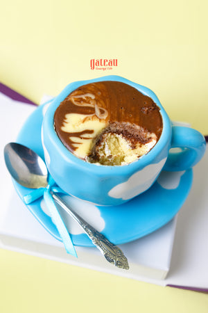Decorative teacup cake in a blue cup with chocolate frosting and a silver spoon at Gateau Gourmet Cafe