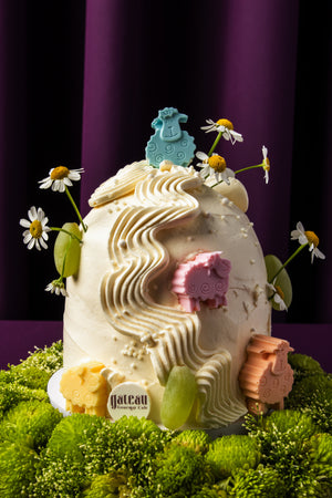 Eid Al Adha cake ideas by Gateau Gourmet Cafe featuring white frosted cake with colorful sheep decorations and flowers