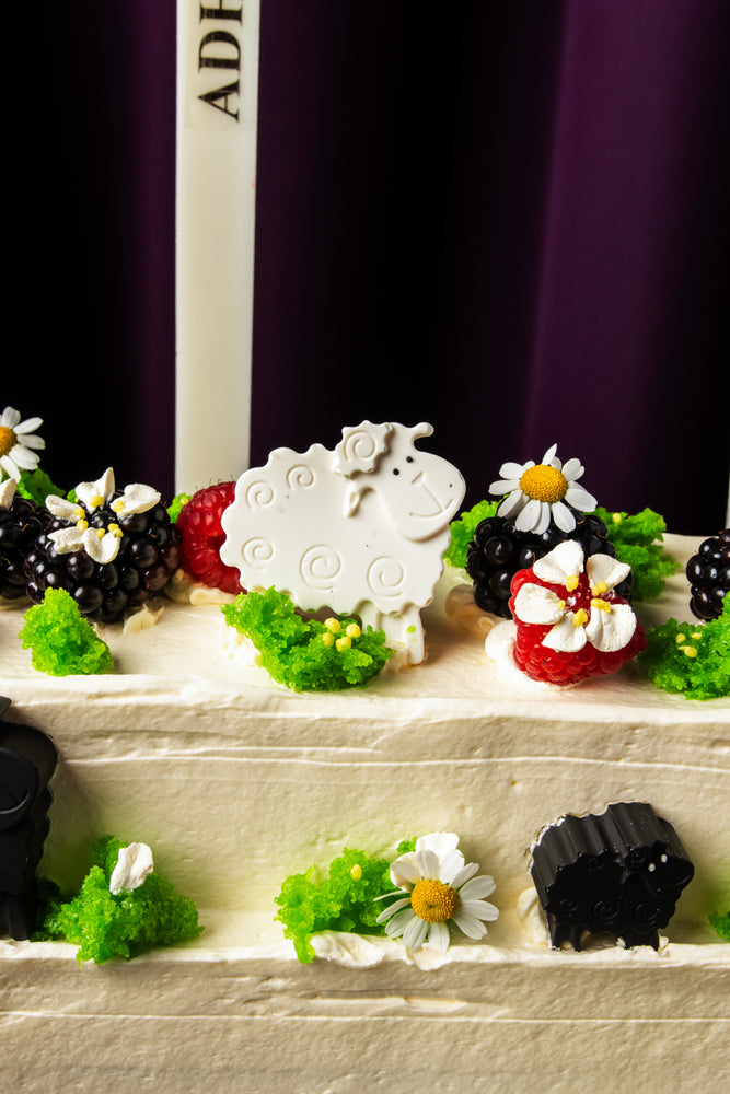 Gateau Gourmet Cafe cake decorated with berries, flowers, and a white sheep for Eid celebration desserts