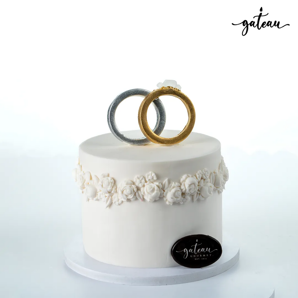 Elegant anniversary cake from Gateau Gourmet Cafe decorated with white floral icing and gold and silver ring toppers