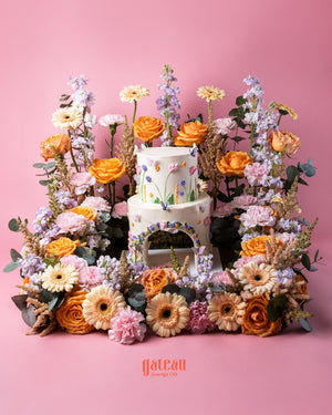 Elegant floral cake arrangement with two-tier white cake surrounded by vibrant orange and pink flowers