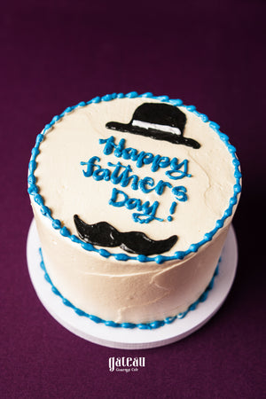 Father's Day mini cake by Gateau Gourmet Cafe with white frosting blue border and black hat and mustache decoration