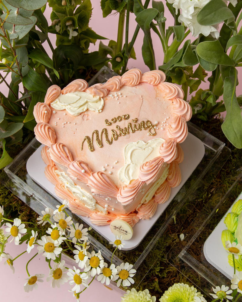 Heart-shaped pink cake with floral cake arrangements and decorative white and peach frosting by Gateau Gourmet Cafe