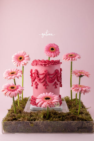 Pink cake with intricate pink floral cake decorations surrounded by fresh pink flowers on moss base