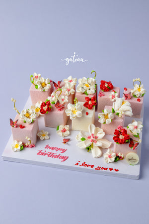 Floral decorated cake cubes by Gateau Gourmet Cafe with intricate red and white flower designs on pink and white bases
