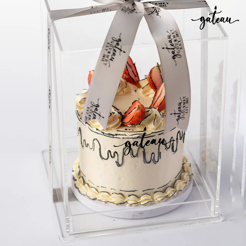 Delicious fresh strawberry cake with creamy frosting and decorative strawberries in a clear display box