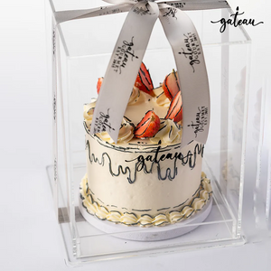 Delicious fresh strawberry cake with creamy frosting and decorative strawberries in a clear display box
