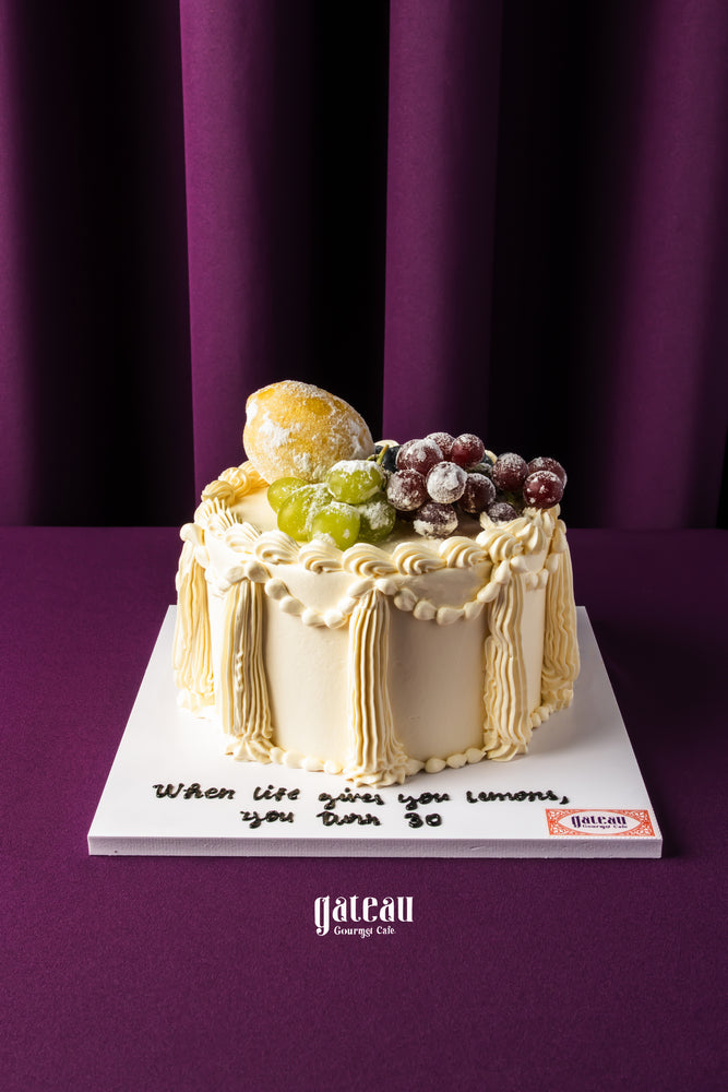 Gateau Gourmet Cafe fruit topped birthday cake with grapes and powdered sugar on elegant vanilla frosting