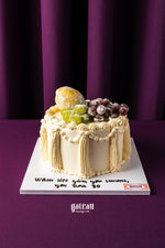 Gateau Gourmet Cafe fruit topped birthday cake with grapes and powdered sugar on elegant vanilla frosting