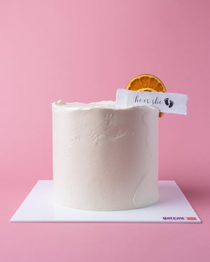 Gateau Gourmet Cafe Gender Reveal Cake with a fresh orange slice and a tag reading he or she
