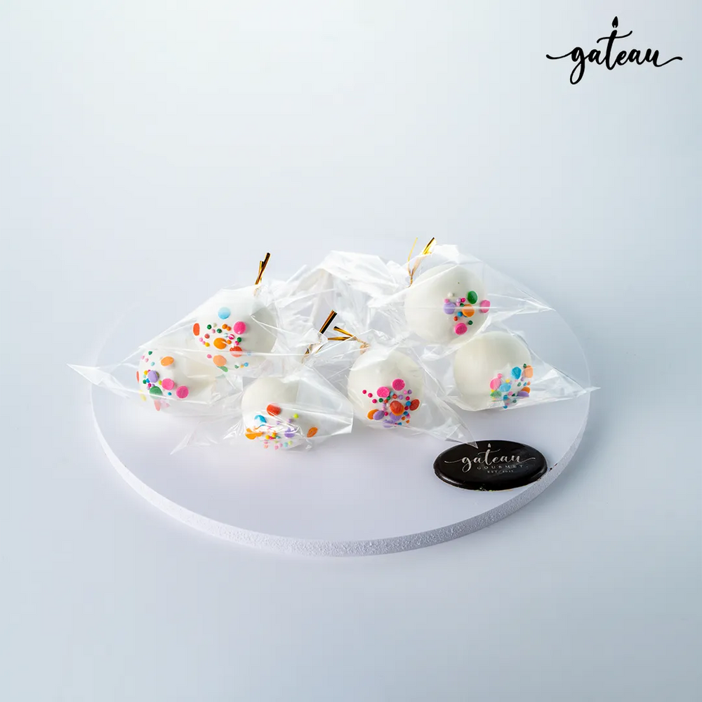 Gateau Gourmet Cafe gourmet cake pops wrapped in clear plastic with white coating and colorful sprinkles on a white round display