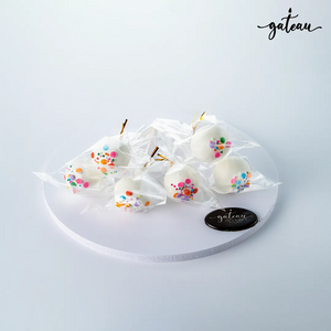 Gateau Gourmet Cafe gourmet cake pops wrapped in clear plastic with white coating and colorful sprinkles on a white round display