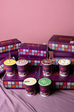 Assorted colorful Gateau Gourmet cups filled with cake and arranged with purple Gateau Gourmet Cafe boxes