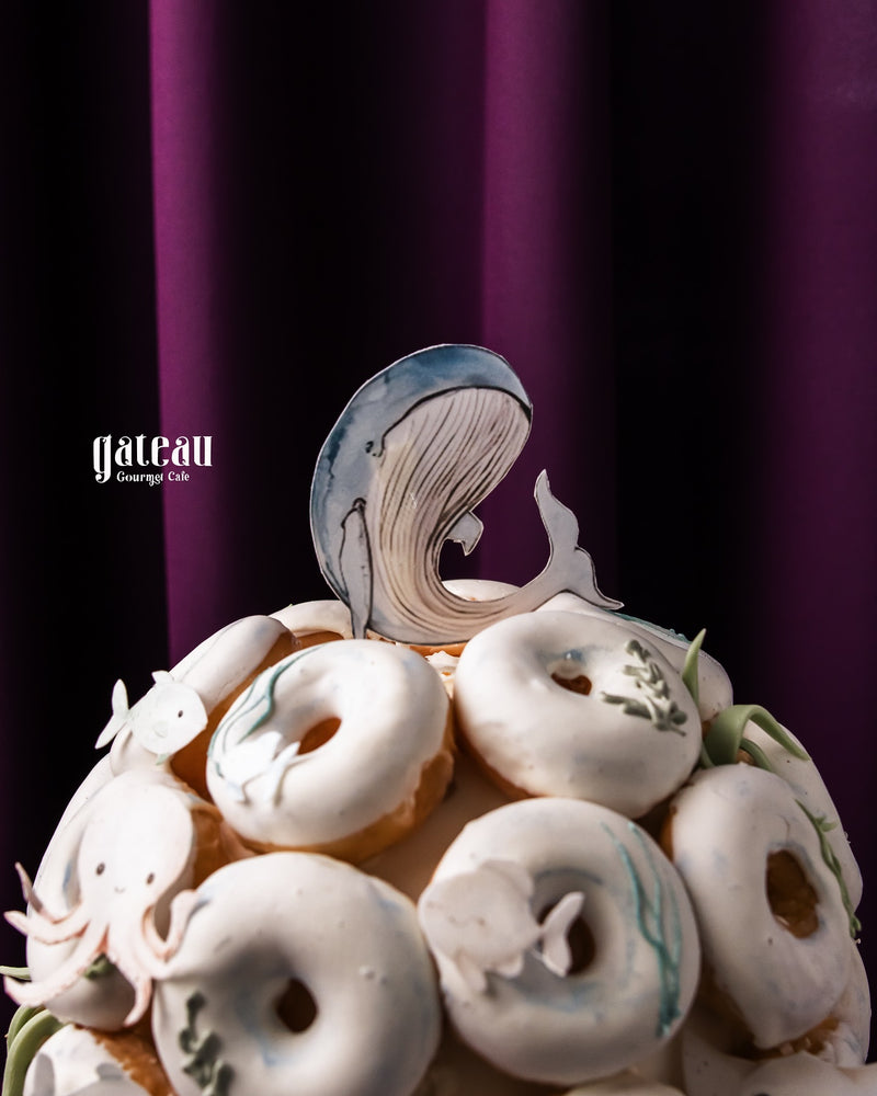Gourmet white-glazed donuts cake with artistic whale topper from Gateau Gourmet Cafe for gourmet donuts delivery