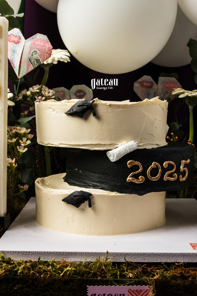 Gateau Gourmet Cafe graduation cake arrangement with black and white tiers, 2025 decoration, and graduation caps