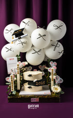 Gateau Gourmet Cafe elegant graduation cake arrangement with white balloons and 2023 cake on dark purple background