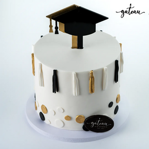 Elegant white graduation cake design with black and gold tassels and a black graduation cap topper